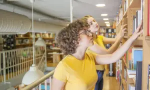 Dwie dziewczyny w żółtych koszulkach przeglądają książki na półkach, szukając inspiracji, jak napisać opowiadanie twórcze.