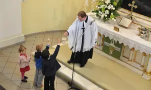 Dzieci z podniesionymi rękami słuchają księdza. Różnice między ewangelikami a katolikami są widoczne w liturgii i symbolach.