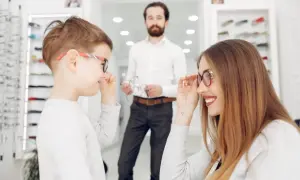 Niños probándose gafas en una óptica. La madre ayuda a su hijo con un **ojo vago** a elegir montura.