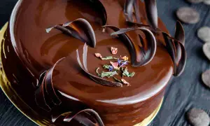 Una lucida torta Savoia al cioccolato, decorata con riccioli di cioccolato fondente e petali di fiori secchi.