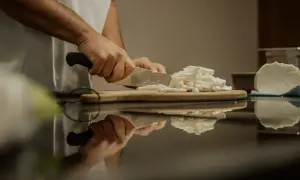 Hände schneiden frischen Käse, eine köstliche fior di latte Alternative, auf einem Holzbrett.