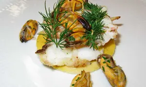 Délicieux plat de joue de lotte poêlée, garni de moules et d'aneth frais, servi sur un lit de purée.