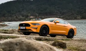 Pomarańczowy Mustang 2.3 Ecoboost z czarnymi felgami stoi nad jeziorem, gotowy na przygodę.