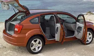 Orange Dodge Caliber 2007 med öppna dörrar och baklucka vid havet. Perfekt för en roadtrip!