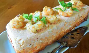 Un délicieux pain de poisson aux crevettes et herbes fraîches, prêt à être découpé avec une pelle à tarte ornée.