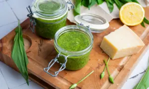 Frisches Bärlauchpesto in Gläsern, bereit für ein köstliches pesto rezept. Daneben ein Stück Parmesan, Zitrone und Bärlauch.