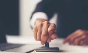 Dłoń z pieczątką, gotowa do złożenia podpisu na akcie poświadczenia dziedziczenia.