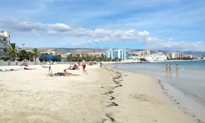 Spiaggia di Manfredonia con persone che prendono il sole e tre donne che camminano nell'acqua cristallina.