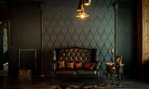 Elegancka skórzana kanapa i stolik tworzą przytulny kącik. Wnętrze w stylu vintage, z tapetą w ornamenty i stylowymi lampami, zaprasza do relaksu.