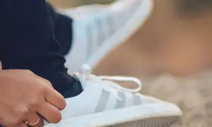 Dłoń z pierścionkiem dotyka białego buta Adidas. Idealna rozmiarówka Adidasa zapewnia komfort.