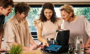 Pięć osób przygląda się ekranowi urządzenia kuchennego, szukając inspiracji na thermomix top 10 przepisów.