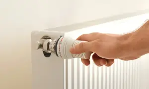 Hand dreht am Thermostatventil eines Heizkörpers. Die Markierungen zeigen eine Einstellung zwischen 2 und 3. Möglicherweise ist der Thermostat defekt.