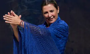 Sara Baras, joven y vibrante, luce un mantón azul eléctrico con flecos, sus manos en un gesto flamenco.