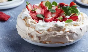 Puszysta beza Pavlova ozdobiona bitą śmietaną, świeżymi truskawkami i listkami mięty. Idealna na letnie popołudnie.