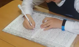 Dziecko pisze długopisem po karcie z zadaniami matematycznymi.