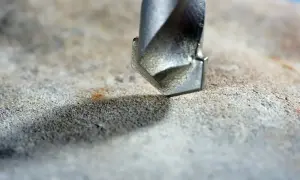 Metalowa wiertarka zbliża się do powierzchni betonu, sugerując wiercenie w betonie bez udaru.