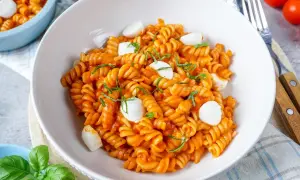 Eine Schüssel mit köstlicher One Pot Pasta, Fusilli in Tomatensauce mit Mozzarella-Kugeln und frischem Basilikum garniert.