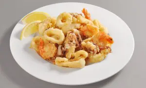 Un invitante piatto di frittura di pesce, con anelli di calamari dorati e gamberi croccanti, guarnito con spicchi di limone fresco.