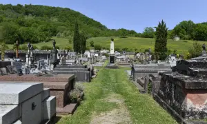 Vue d'un cimetière avec des tombes et des croix, sur fond de colline verdoyante.