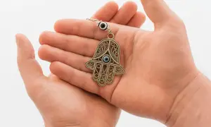 Dłonie trzymają ozdobny amulet ręka Fatimy z niebieskim okiem.