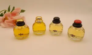 Cztery miniaturowe flakoniki perfum YSL Paris, obok delikatnych różowych kwiatów.