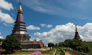 Dwa pagody na szczycie Doi Inthanon National Park, otoczone kwitnącymi kwiatami i bujną zielenią, pod błękitnym niebem z białymi chmurami.