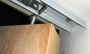 Detalle de una puerta armario descolgada, con el soporte metálico visible y el borde de madera.