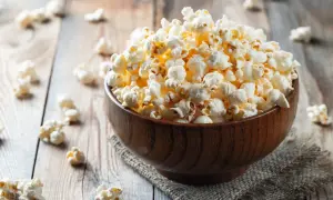 Pełna miska popcornu na drewnianym stole. Czy zastanawiasz się nad popcorn kcal?