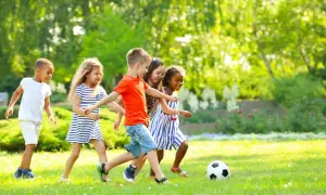Kinder haben Spaß bei Bewegungsspielen im Kindergarten. Sie spielen Fußball auf einer sonnigen Wiese.