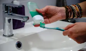 Ręka z kolorowymi bransoletkami nakłada zieloną pastę na szczoteczkę do zębów. Czas na poranne mycie zębów!