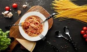 Talerz spaghetti z sosem pomidorowym, czosnek, pomidory, bazylia i parmezan. Takie składniki sugerują, skąd pochodzi spaghetti.