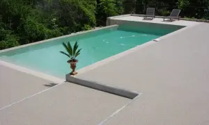 Piscina con bordo in cemento e pavimentazioni in cemento a vista, circondata da vegetazione lussureggiante.