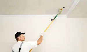 Un peintre utilise un rouleau à long manche pour peindre un plafond, suivant un schéma précis pour un résultat parfait.