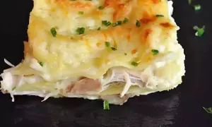 Une part de lasagnes poulet champignons, gratinée et garnie de persil frais, sur une assiette noire.