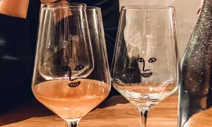 Dwa kieliszki z zabawnymi buźkami na drewnianym stole w wine barze w Gdańsku. Jeden z nich zawiera różowe wino.