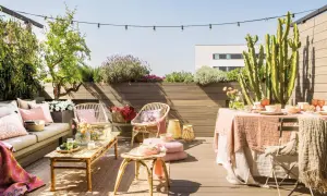 Terraza de ático lista para disfrutar. Una reforma que invita a la relajación con mobiliario de ratán, textiles suaves y plantas exuberantes.