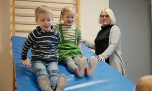 Zwei Kinder rutschen auf einer blauen Matte, während eine Erzieherin zusieht. Ein Fall könnte eine aufsichtspflichtverletzung kita darstellen.