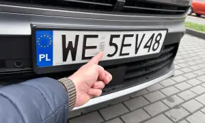 Dłoń wskazująca na hologram na polskiej tablicy rejestracyjnej samochodu.