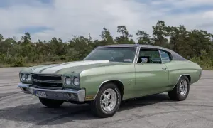 Grön Chevelle SS från 1970 med vita ränder på huven, parkerad utomhus med träd i bakgrunden.