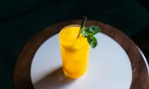 Orzeźwiający drink z mango, z kostkami lodu i listkiem mięty, podany w szklance ze słomką.