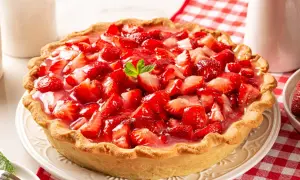 Pyszna tarta z truskawkami, obficie udekorowana świeżymi owocami i galaretką, prezentuje się apetycznie na talerzu.