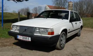 Białe Volvo 840 z przodu, na tle drzew i kościoła.