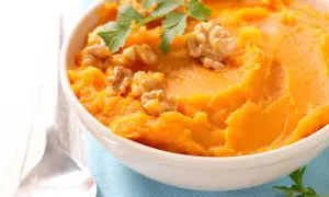 Un bol de purée de patate douce onctueuse, garni de noix croquantes et de persil frais. Un délice réconfortant.