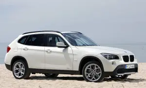 Białe BMW X1 E84 na piaszczystej plaży, z widokiem na morze w tle.