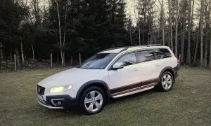 Vit Volvo XC70 parkerad på en gräsmatta med skog i bakgrunden. Kanske ett volvo d4 motor problem gör att den står stilla.