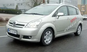 Srebrna Toyota Corolla Verso jedzie po mokrej drodze. Na drzwiach widnieje napis "Toyota Corolla Verso".