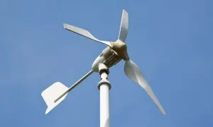 Moja elektrownia wiatrowa, biała turbina z trzema łopatami, obraca się na tle błękitnego nieba, czerpiąc energię z wiatru.