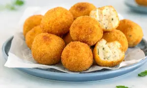 Un piatto di polpette di ricotta dorate e croccanti, alcune intere, altre spezzate per mostrare il ripieno morbido e profumato.