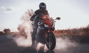 Motocyklista w kasku i kombinezonie na pomarańczowym Barton Blade 125, z którego wydobywa się dym. Zastanawiasz się, ile pali motor 125?