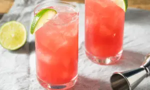 Dwa orzeźwiające drinki z likierem Passoa, lodem i plasterkami limonki. Obok leży połowa limonki i miarka barmańska.